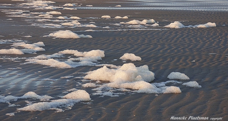 In de wind rolt het schuim over het strand